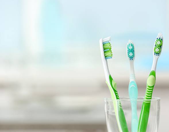Three toothbrushes in a clear plastic cup
