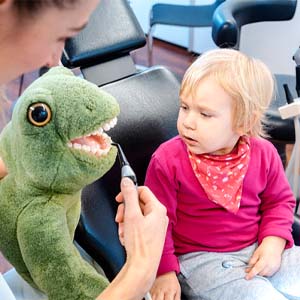 dentist using stuffed animal to explain cleaning to patient