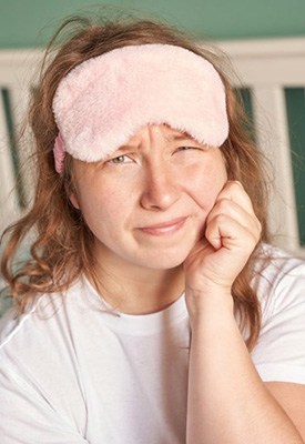 Woman with sleep mask rubbing her aching jaw