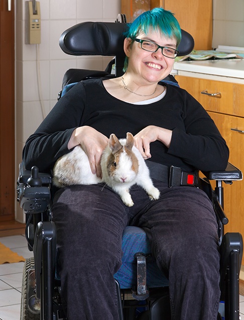 Woman in wheelchair smiling after treatment to replace missing teeth